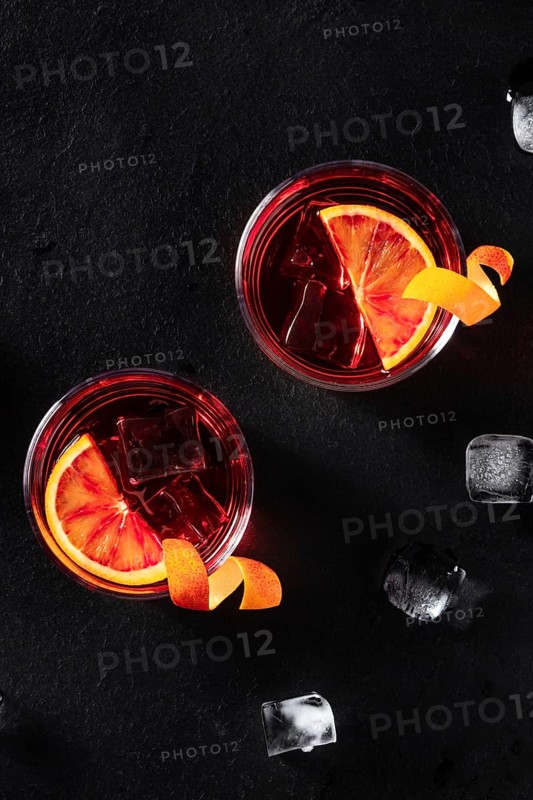 Negroni cocktails with orange rind, shot from the top with ice cubes on a black background, with copy space