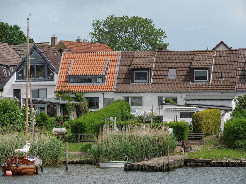 Terraced houses with well-kept gardens and boats along a riverbank in a quiet residential area, holm, schleswig. germany