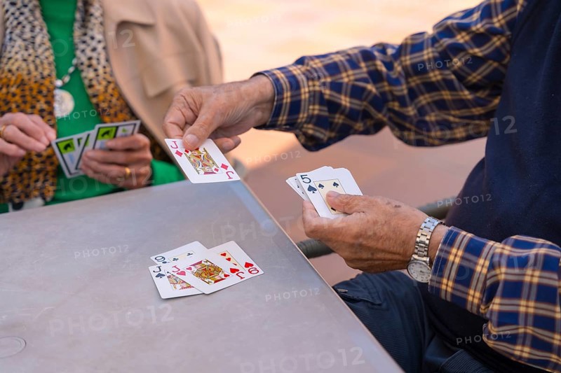 Hands of two elderly people in the garden of a nursing home or retirement home playing cards on a summer morning