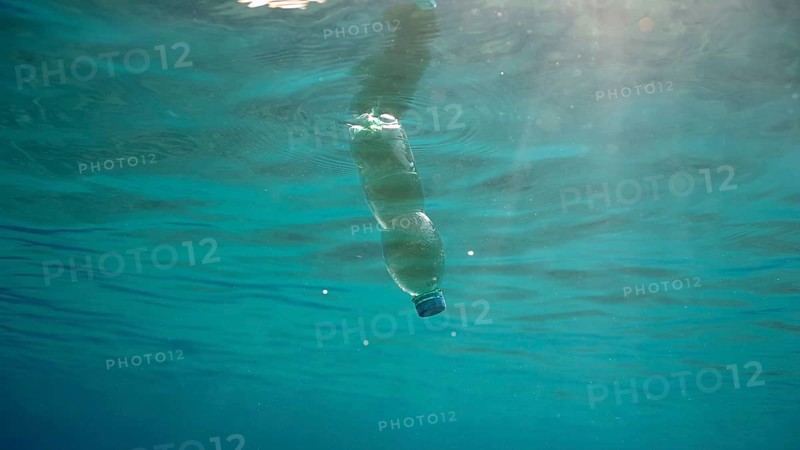 Green plastic bottle drifting under surface of blue water. Plastic pollution of Ocean, Discarded plastic bottle floats underwater in sunlight, Red sea, Egypt, Africa