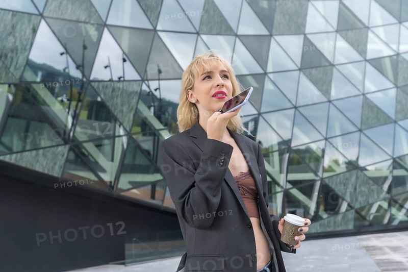 Entrepreneurial girl business park in a modern building with colored glass, young blonde woman in suit sending a voice note