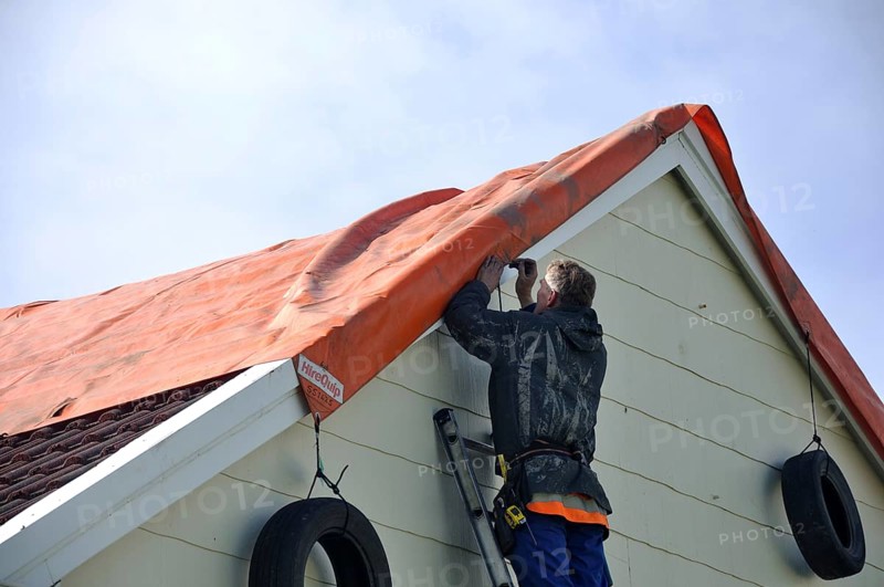 GREYMOUTH, NEW ZEALAND, APRIL 17, 2014: Volunteer worker places a tarpaulin on a house de-roofed in Cobden by Cyclone Ita, Greymouth, New Zealand, April 17, 2014, Oceania