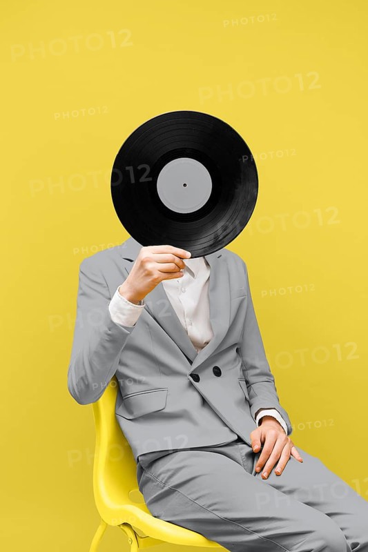 Man covering his face with vinyl record while wearing ultimate gray clothes. High resolution photo