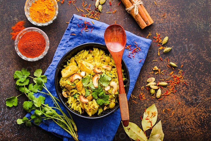 Biryani rice, traditional Indian dish. Biryani spicy rice, chicken, nuts. Indian rice bowl, spices, herbs, rustic stone background. Top view. Space for text. Asian style biryani rice. Indian dinner