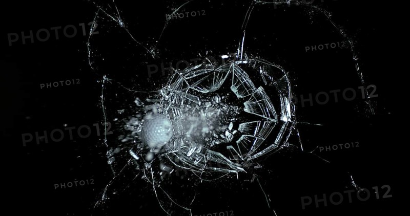 Golf Ball breaking Pane of Glass against Black Background