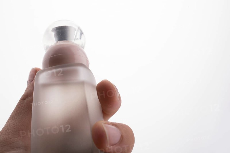 Little perfume glass bottle in hand on a white background