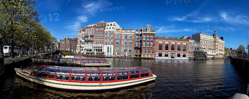 City tour ships are anchored at the Amstel in Amsterdam, Netherlands in spring. City tour ships anchored on the Amstel in Amsterdam, Netherlands in springtime