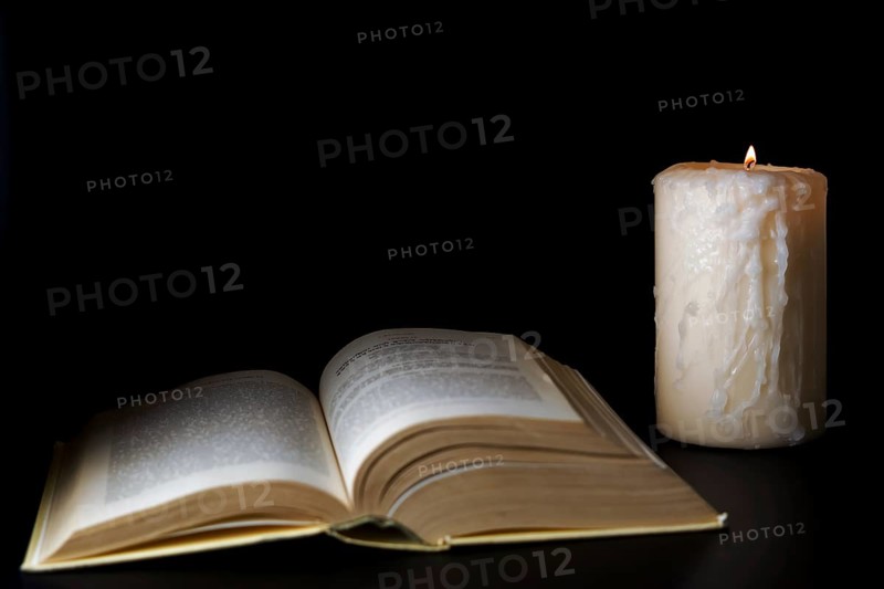 Open book illuminated by candlelight isolated on a black background