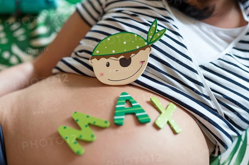 A wooden replica of a baby boy's face and letters for the name Max lie on a pregnant woman's belly