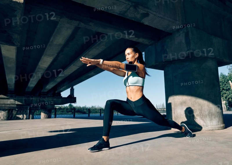 Young sporty woman doing yoga asana Warrior I Pose outdoors under industrial bridge. Practicing yoga, wellbeing and healthy lifestyle. Virabhadrasana
