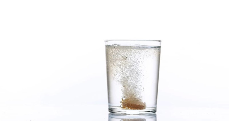 Tablets Falling and Dissolving into a Glass of Water against White Background