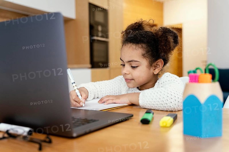 Little girl home studying during online school with laptop
