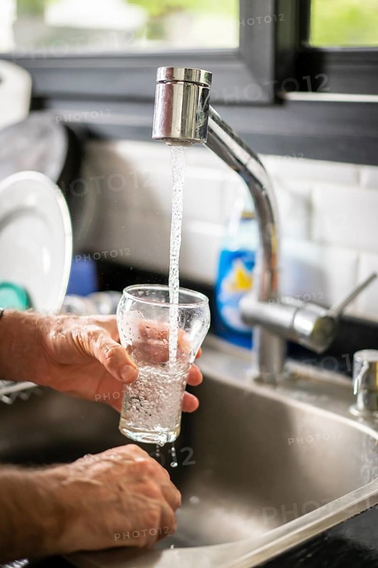 Man pouring water into glass in kitchen, closeup