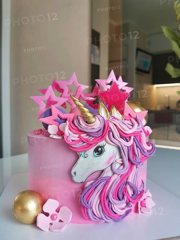 A whimsical unicorn birthday cake with pink and gold decorations, featuring pastel flowers and star accents