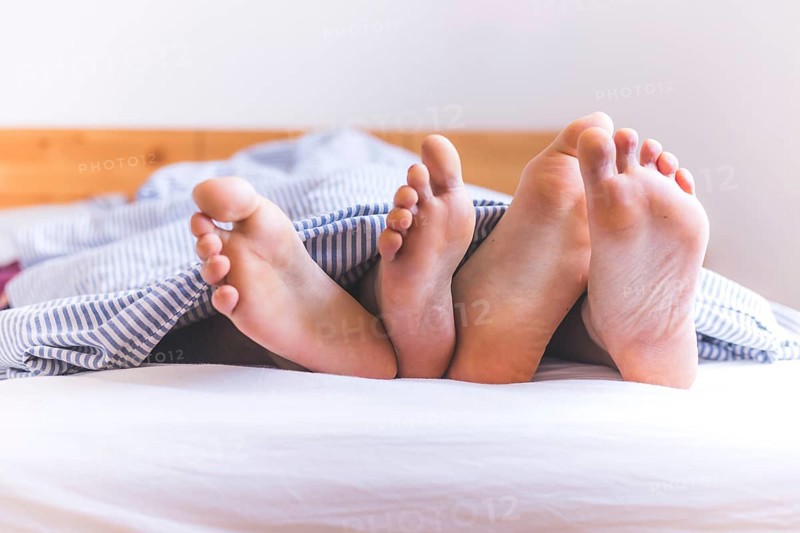 Close up a couples uncovered feet sleeping in bed, morning