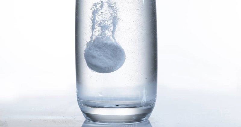 Tablets Falling and Dissolving into a Glass of Water against White Background