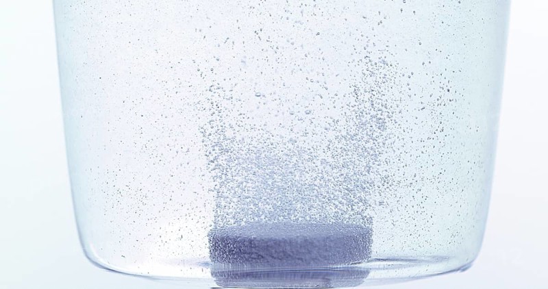 Tablets Falling and Dissolving into a Glass of Water against White Background