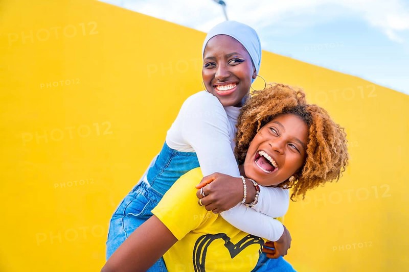 Happy scene of a muslim woman piggybacking an african friend outdoors