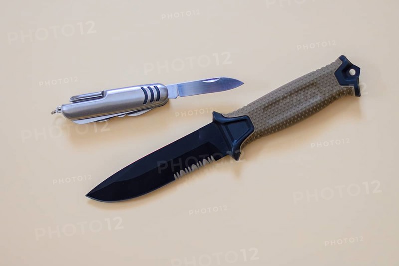 A hunting knife with a beige handle lies next to a Swiss Army knife on a cream-coloured surface