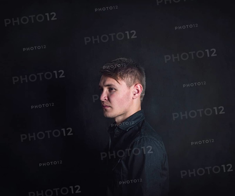 Thoughtful young man side view portrait, looks upset and tired against a dark wall background. Stressed male student feels emotional discomfort and anxiety problems