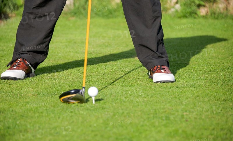 Golfer addresses golf ball with driver in tee box