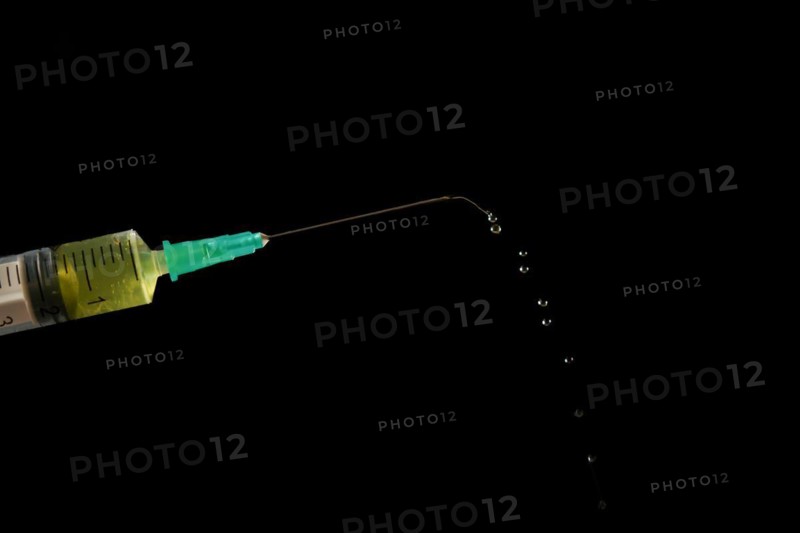 Syringe with needle, a row of drops of yellow liquid coming out, isolated on black background and copy space