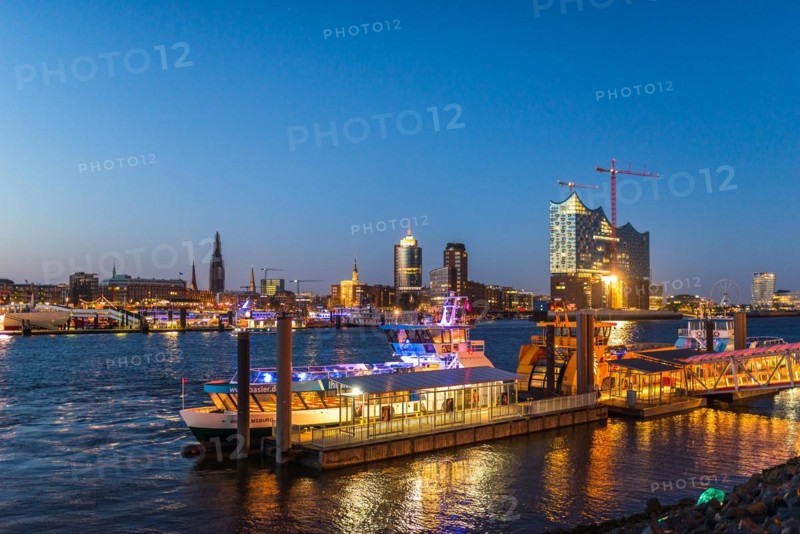 Night picture from the illuminated skyline of Hamburg at the Elbe river with the attractions Elbe Philharmonic Hall and parts of the new HafenCity. In the foreground the pier with local traffic ferries at the musical theater King of the Lions. Hamburg is the city with the most musical theater in Germany