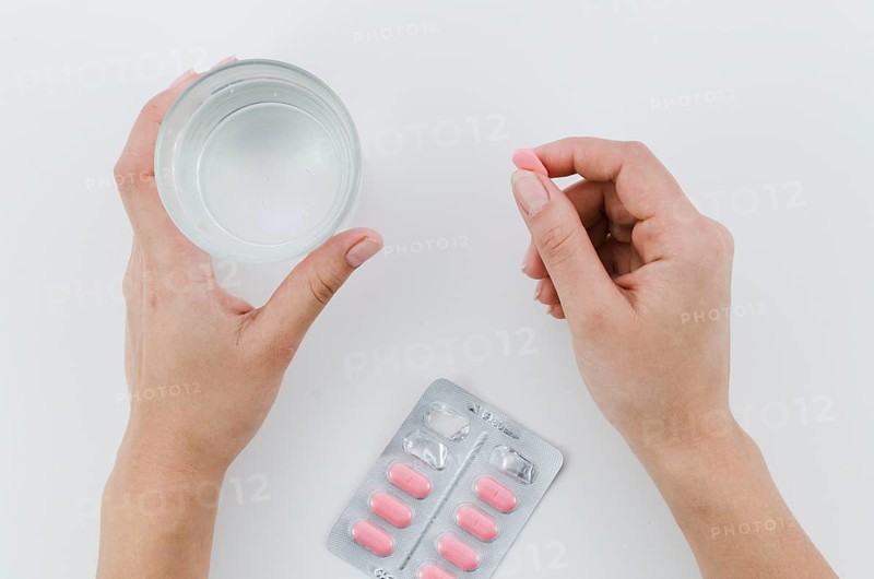 Close up woman s hand holding pink pills glass water white background