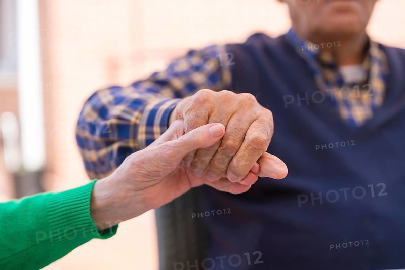Detail of the hands of two elderly people in the garden of a nursing home or retirement home holding hands in a moment of affection