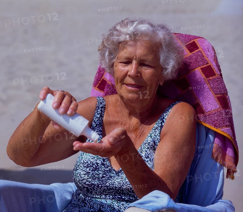 Old woman with sun cream on the sandy beach
