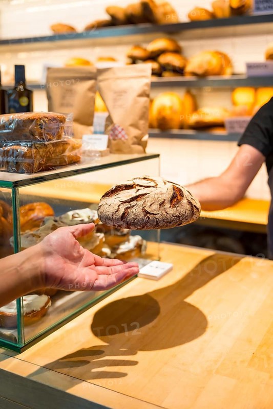 Hands of customer in the bakery shop buying an artisan bread from the baker in the workshop, vertical photo