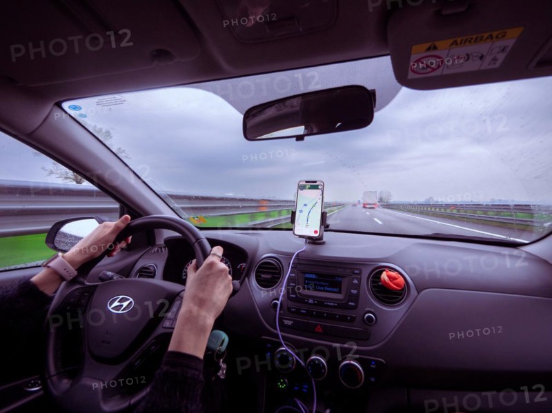 Driver's view from inside a car with a phone showing navigation on a cloudy day, A1 A8 highway near Milan, Italy, Europe
