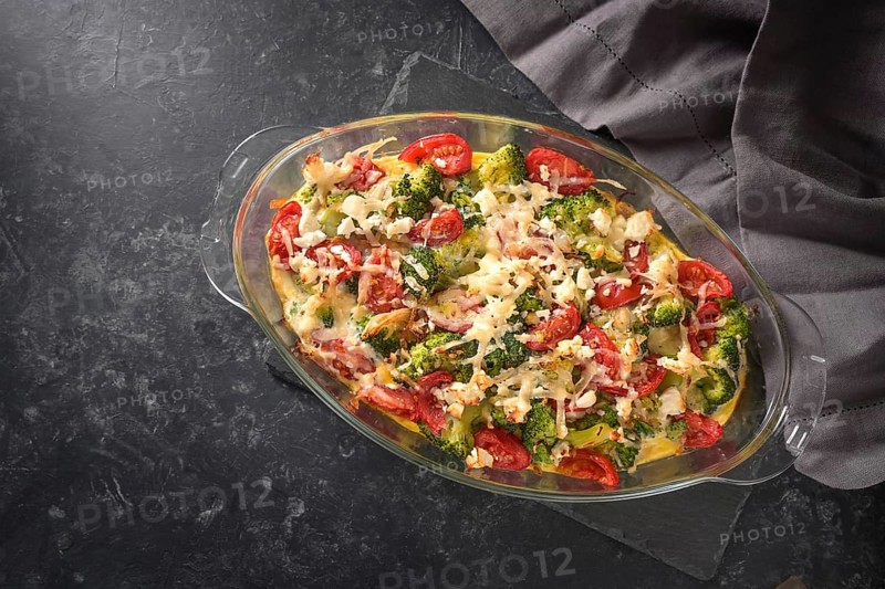 Casserole from broccoli, tomatoes, onions, feta and cheese, healthy vegetable dish on a dark gray slate background, high angle view from above, copy space, selected focus, narrow depth of field