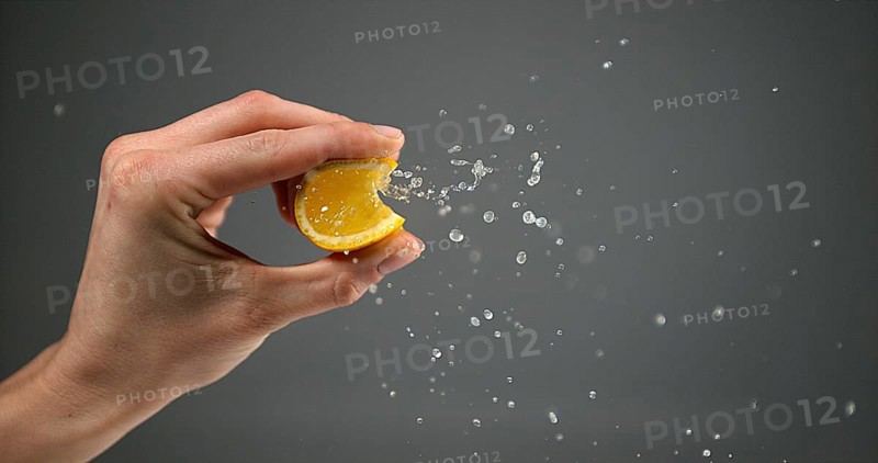 Hand of Woman Squeezing Orange against Black Background