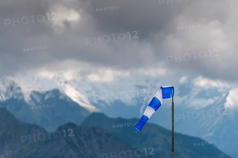 Blue and white windsock on the summit of the Nebelhorn in front of the mountain range with dark clouds