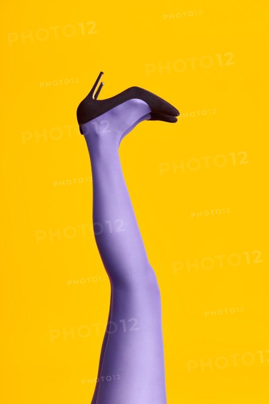 Raised females legs in bright tights and stylish high heels shoes on yellow background. Relax, glamour, pop art concept