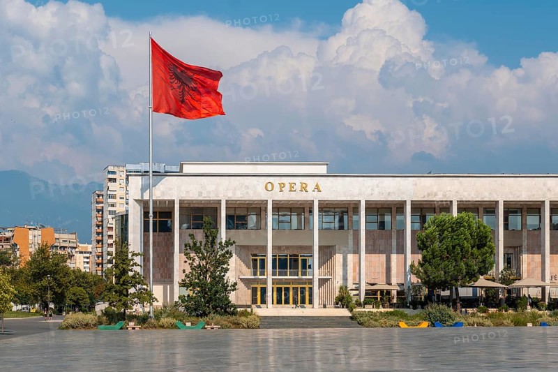 Palace of Culture or Opera on Skanderbeg Square in Tirana and the flag of Albania moving in the wind