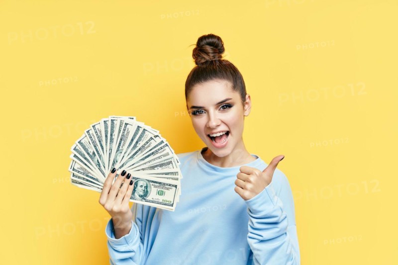 Happy excited young woman showing money banknotes with thumbs up on yellow background. Motivation, success concept