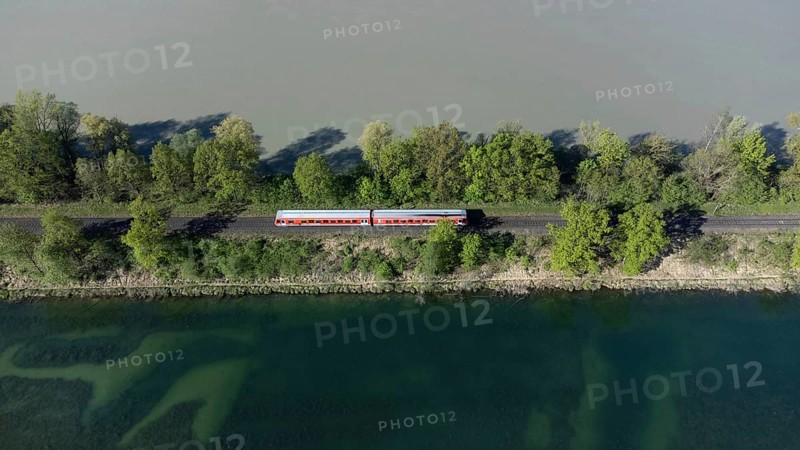 A red local railway runs on an embankment between two bodies of water with different colours, drone shot, Upper Bavaria, Bavaria, Germany, Europe