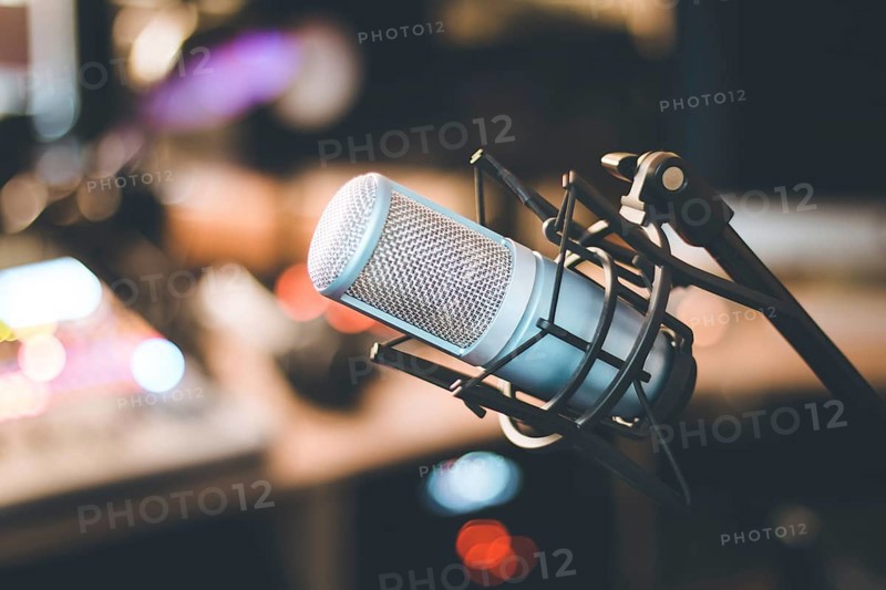 Microphone in a professional recording or radio studio, equipment in the blurry background