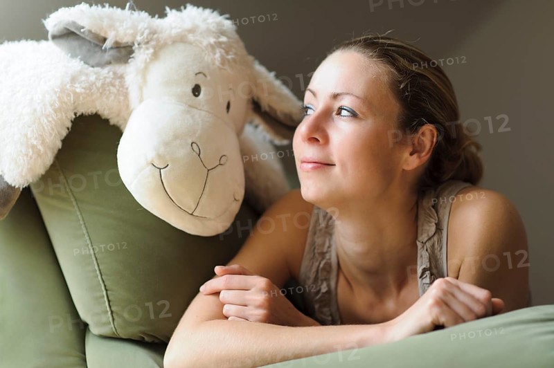 Young woman lying on the couch with a soft toy
