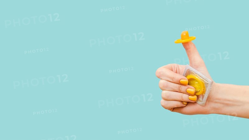 Woman holding yellow condom her finger