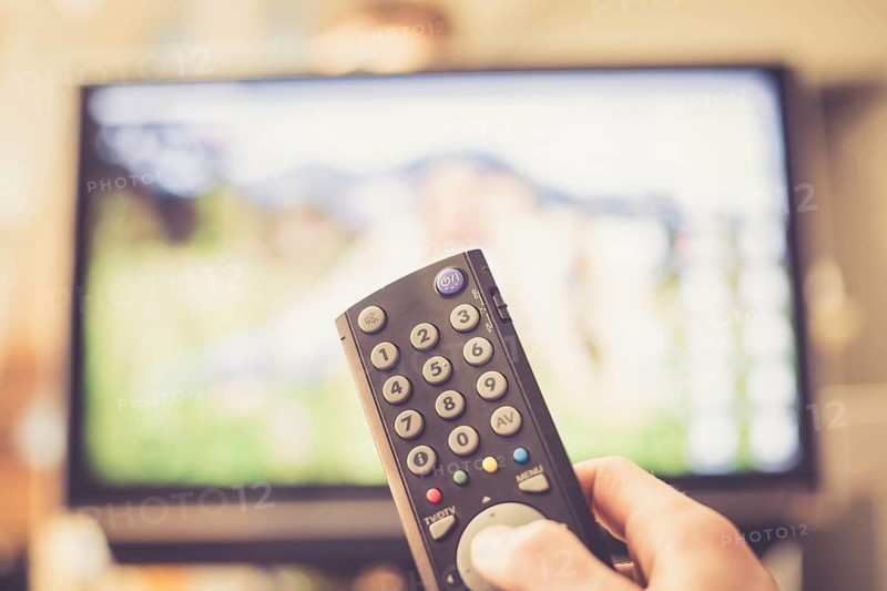 TV remote control in the foreground, tv in the blurry background. Film night with vod streaming
