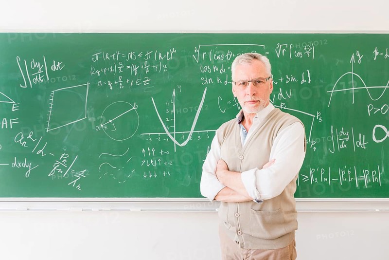 Elder professor standing near chalkboard classroom