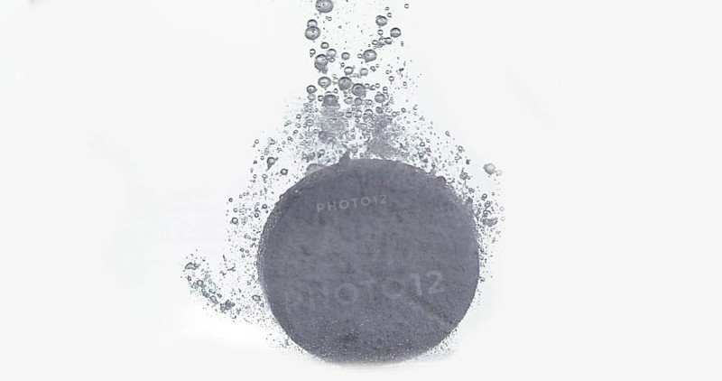 Tablets Falling and Dissolving into a Glass of Water against White Background