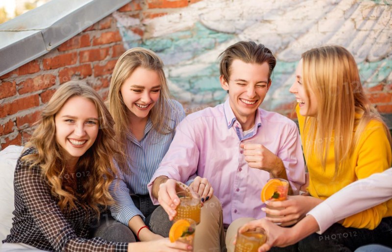 Group of young happy people friends drinking fruit cocktails together on house terrace, smiling and laughing, group of teenagers expressing positive emotions and having fun on party