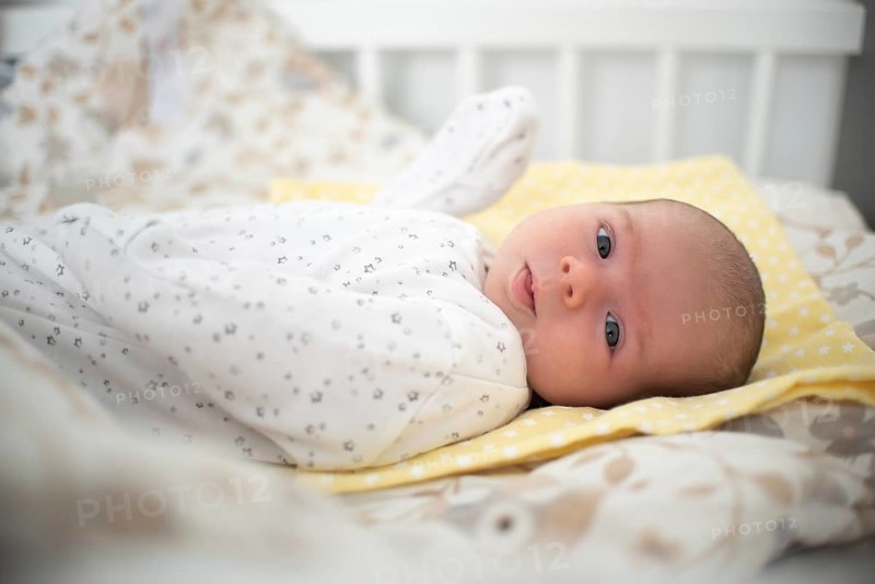 Newborn baby is lying on its side in baby crib in bright room