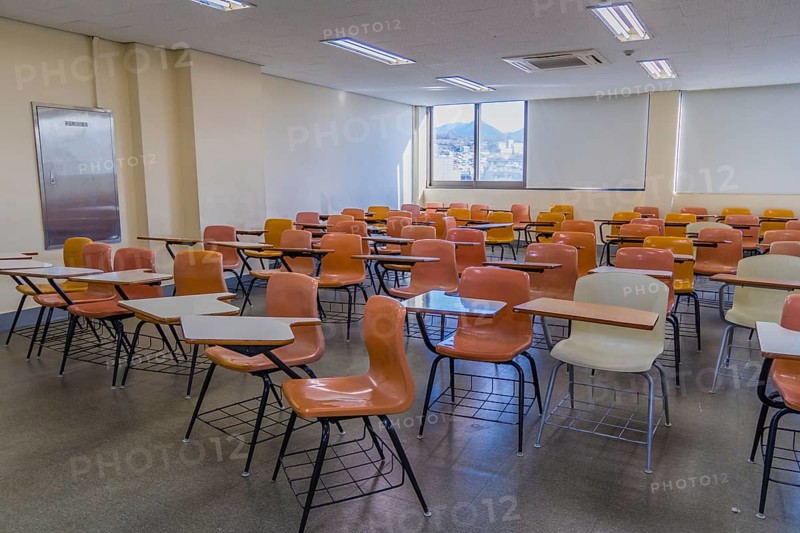 Classroom with empty desks arranged haphazardly with lights turned on and sunshine coming through one window, South Korea, South Korea, Asia