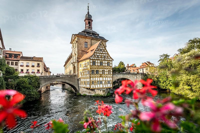 Colourful half-timbered house on a bridge with foreground of bright flowers over a river, old town hall Bamberg Bamberg