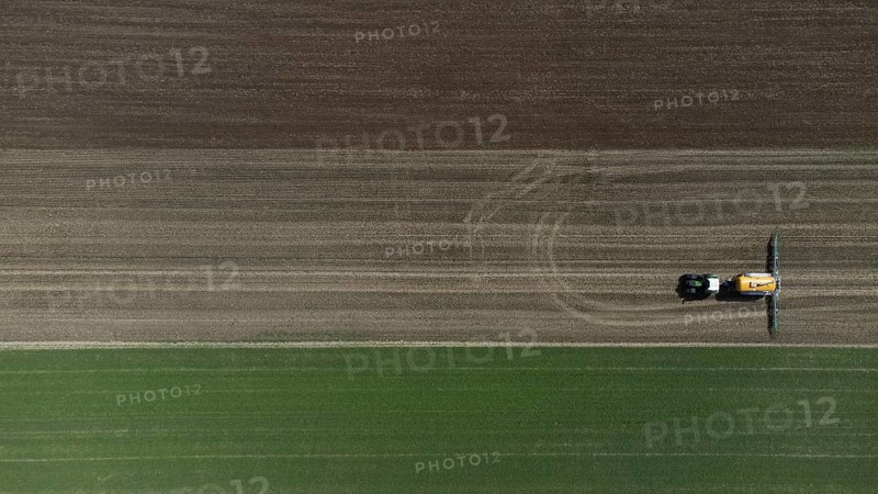 A green tractor with a yellow slurry tanker fertilises a harvested field, bird's eye view, drone shot, Lower Bavaria, Bavaria, Germany, Europe